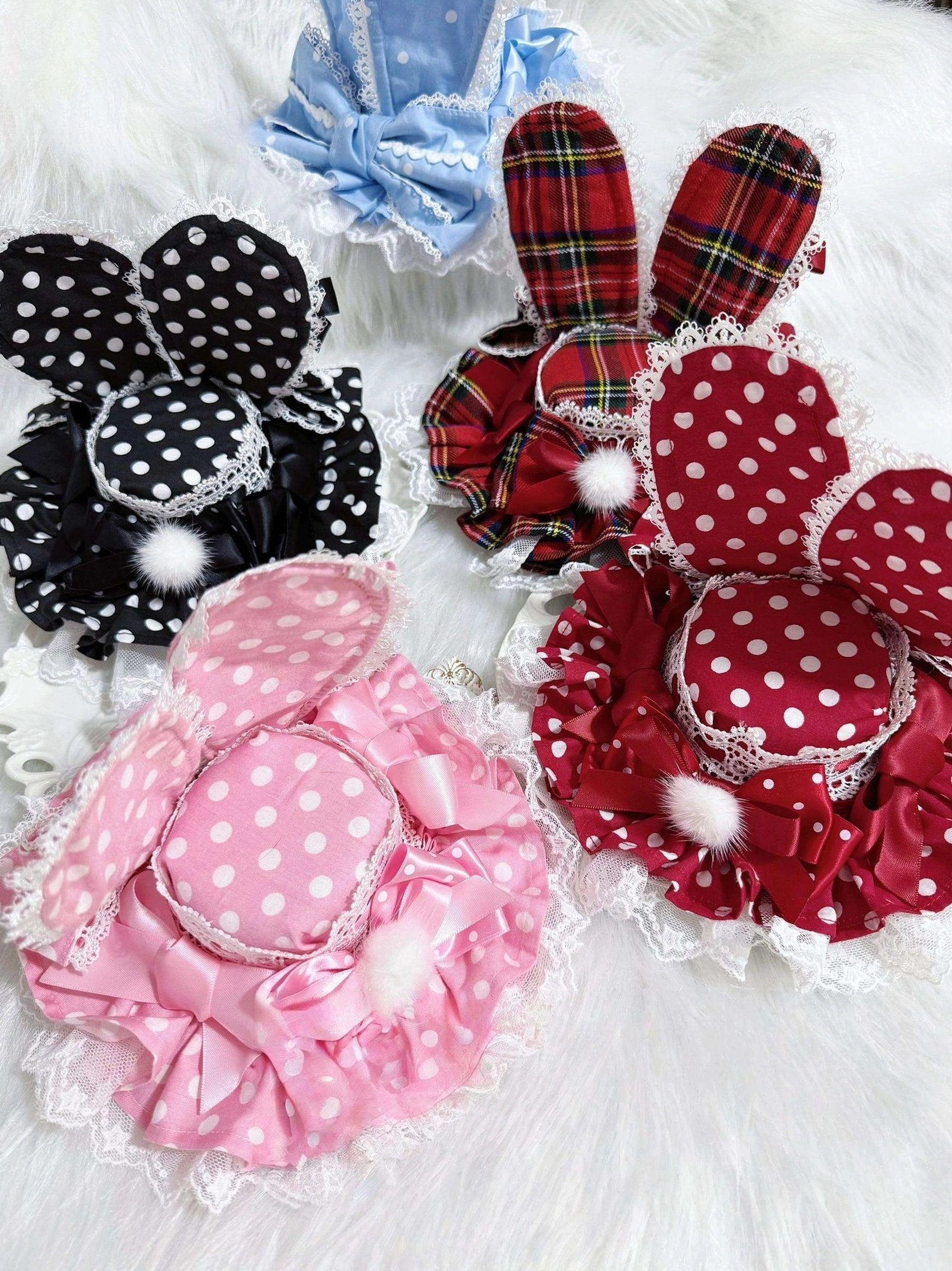 Kawaii Lolita bunny ear hair clip headdress collection flat lay featuring polka dot red, pink, blue and plaid styles with lace trim and pom-pom decorations on white fuzzy background
