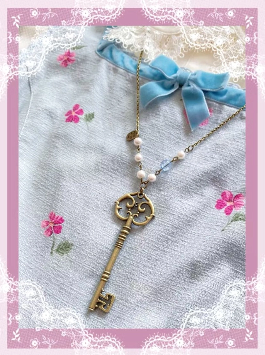 Key pendant Lolita necklace with bronze key charm and tiny metal tag accent on beaded chain displayed over floral Lolita dress collar with lace border