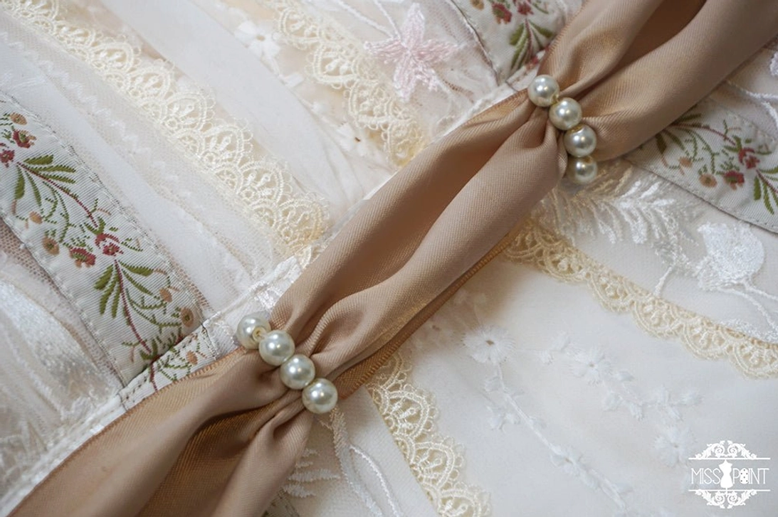 Close-up side flat lay of khaki satin lolita ribbon belt tied with clustered pearl decorations on embroidered floral dress fabric background