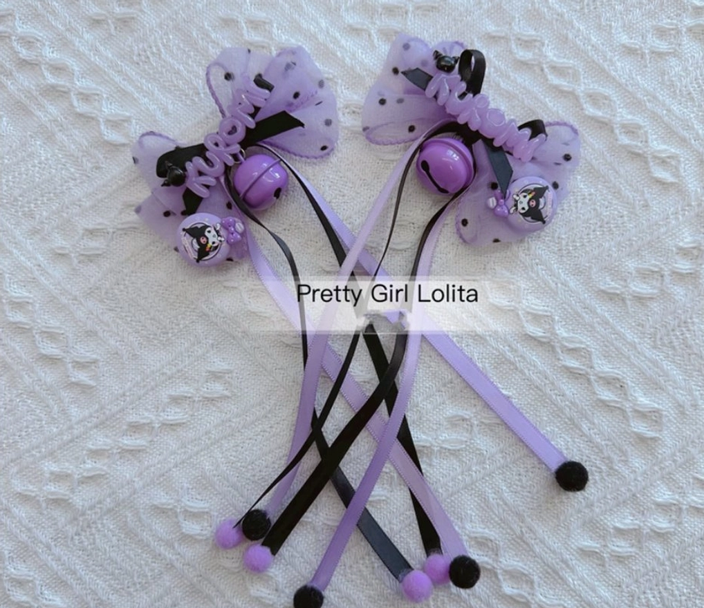 Pair of Kuromi hair clips with long purple polka dot tulle streamers purple bells and Kuromi badge pom-pom decorations overhead flat lay