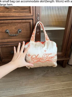 Large champagne Lolita dress storage bag held in front of a wooden cabinet, showing its spacious capacity, embroidered detail, and practical carry straps