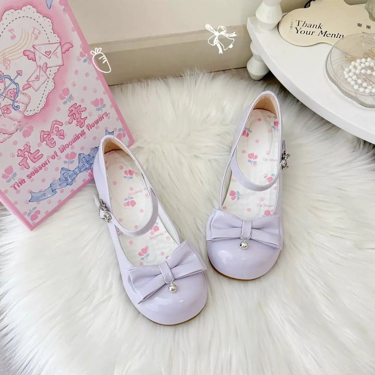 Lavender purple glossy patent leather sweet lolita Mary Jane shoes featuring pearl-accented front bow, silver ankle buckle strap, printed floral insole, and signature cat paw-shaped block heel, set on white fur rug with coordinating branded packaging and vanity shelf styling