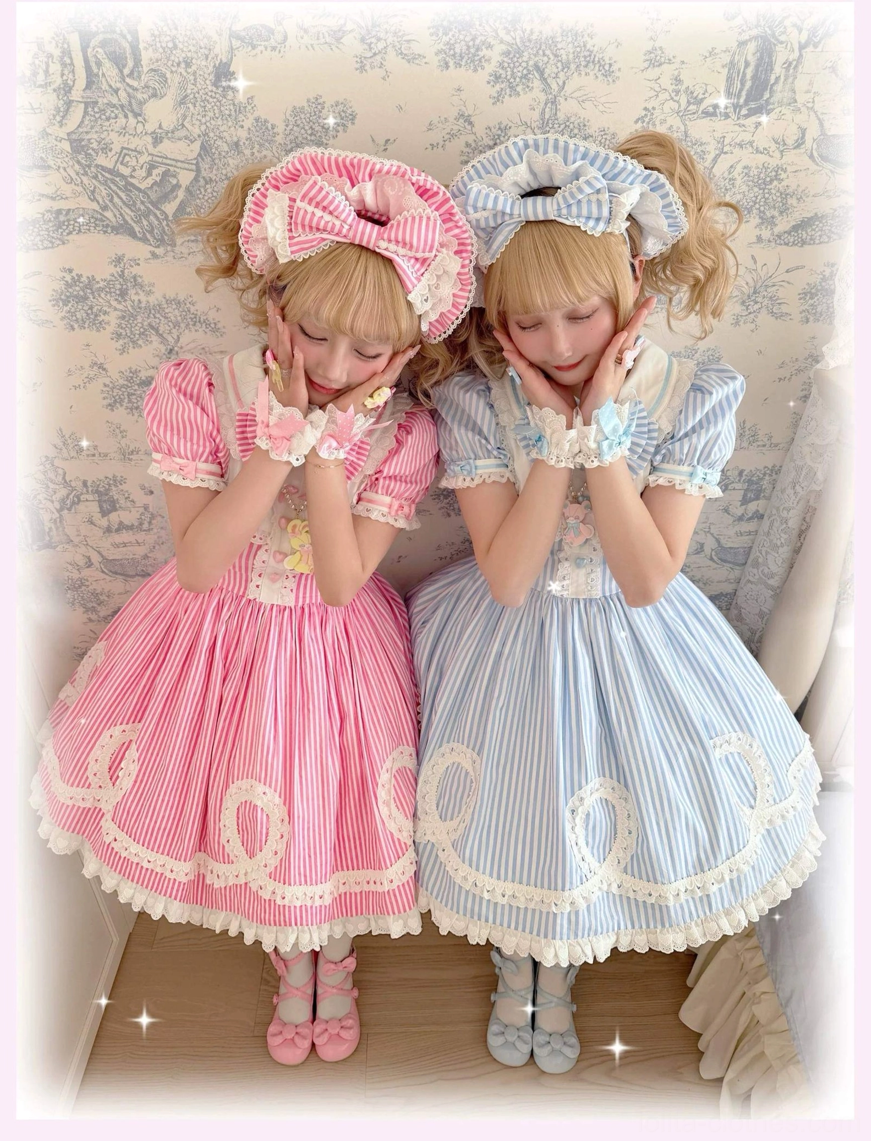 Two leaning female models wearing pink and blue striped old school lolita OP dresses with matching shoes and twin blonde hairstyles in vintage interior