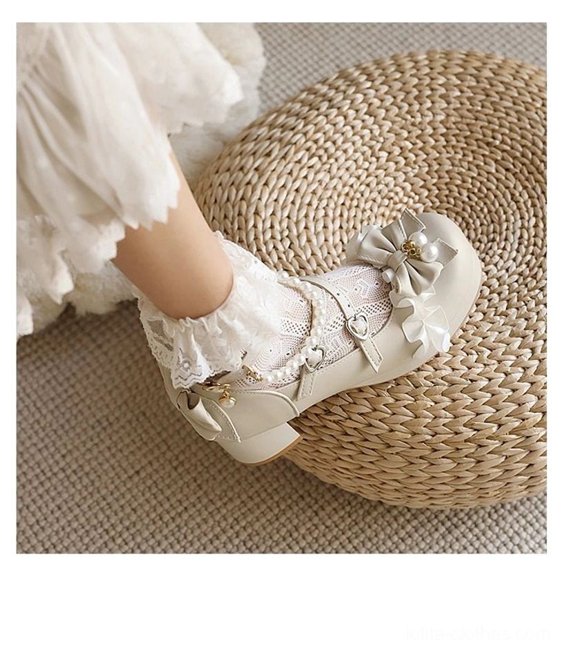 Light beige round-toe sweet lolita shoes low angle close-up of model's foot on woven rattan mat showing bow with pearl decoration, detachable pearl cross strap chain, ruffle flower accent on rounded toe, soft smooth leather upper