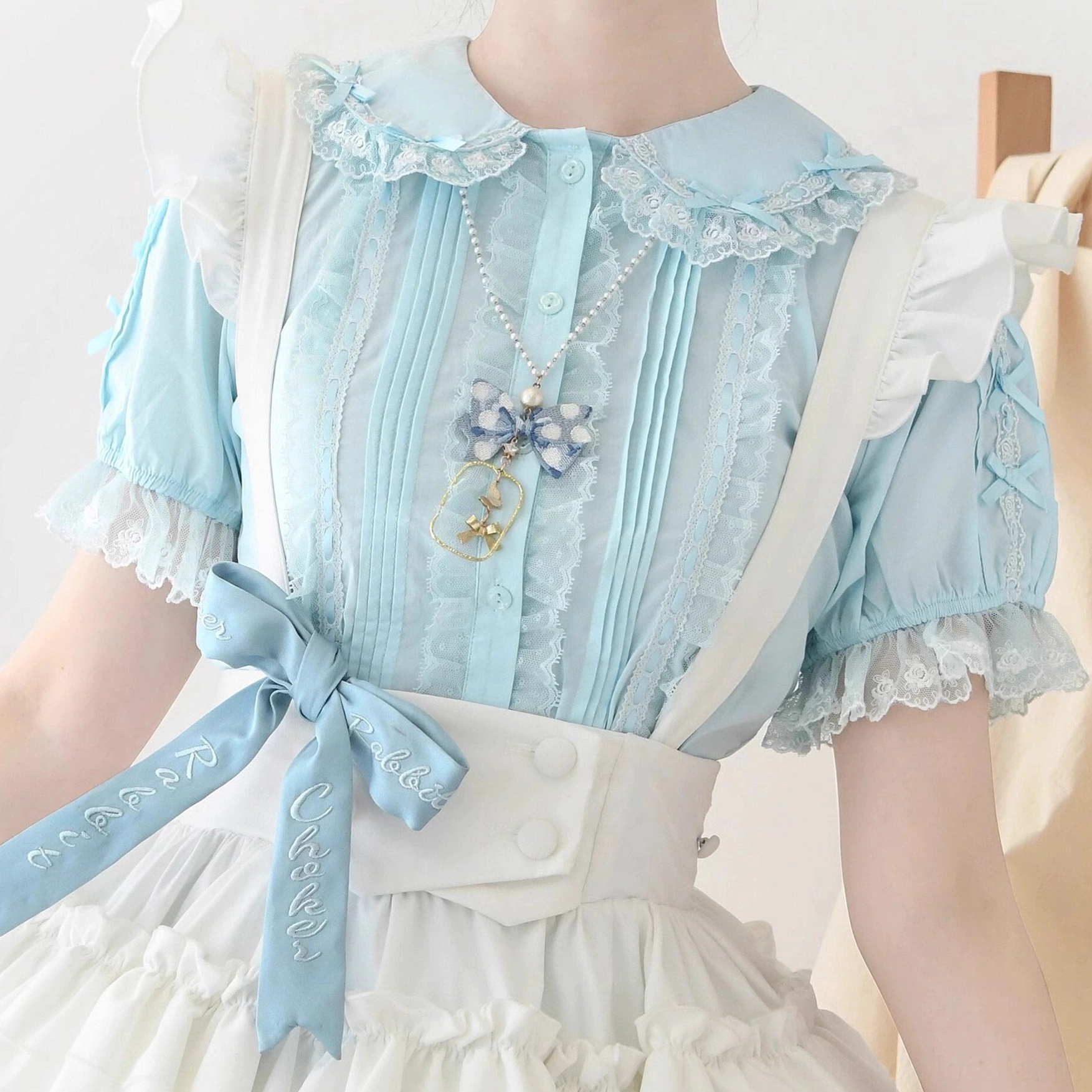 Torso close-up light blue lolita blouse on model paired with waist belt and brooch showing ruffled lace sleeves collar