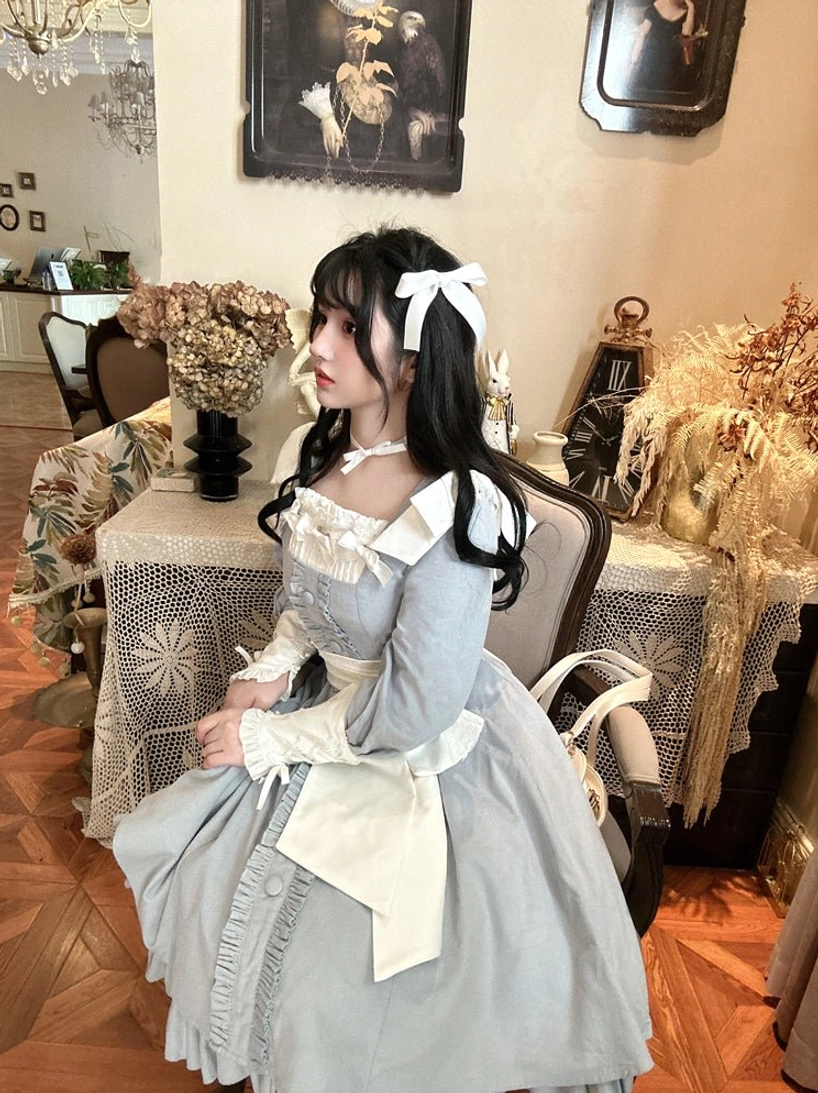 Light blue maid-style Lolita OP dress side half-body shot in retro dining room with dried flower ornaments, featuring white ruffled apron, white hair bow, contrast white cuffs and chest frills