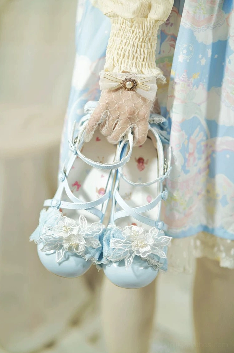 Light blue pastel patent leather sweet Lolita heels held in model's hands showing round toe silhouette floral bow appliques and cross ankle straps, model wearing lace cuff and printed skirt