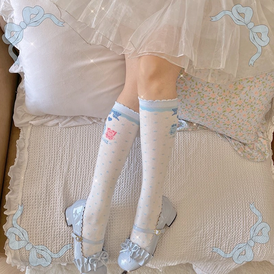 Light blue ruffled lolita calf socks paired with silver Mary Janes and white tulle skirt on cozy bedroom bed with floral pillows