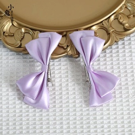 Light blue Sweet Lolita satin bow hair clips front view on blonde curly wig with wooden stand showing soft sky blue satin fabric and paired clip styling
