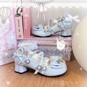 Light blue sweet lolita Mary Jane heels with ruffled ankle straps, heart-shaped metal buckles, and back bow with heart ornament displayed on wooden table with themed shoeboxes