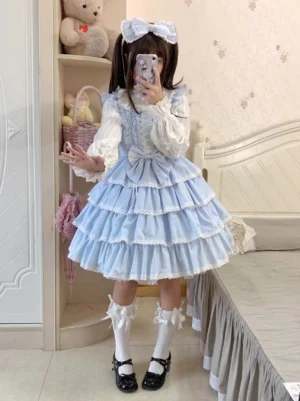 Light blue solid color sweet lolita JSK jumper skirt with tiered ruffled lace hem and front lace-up bow bodice, full-body front view on female model wearing matching twin-tailed hair bow