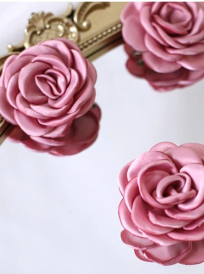Close-up flat lay of light pink and ivory fabric rose accessories showing delicate layered petal structure and pearlescent satin finish