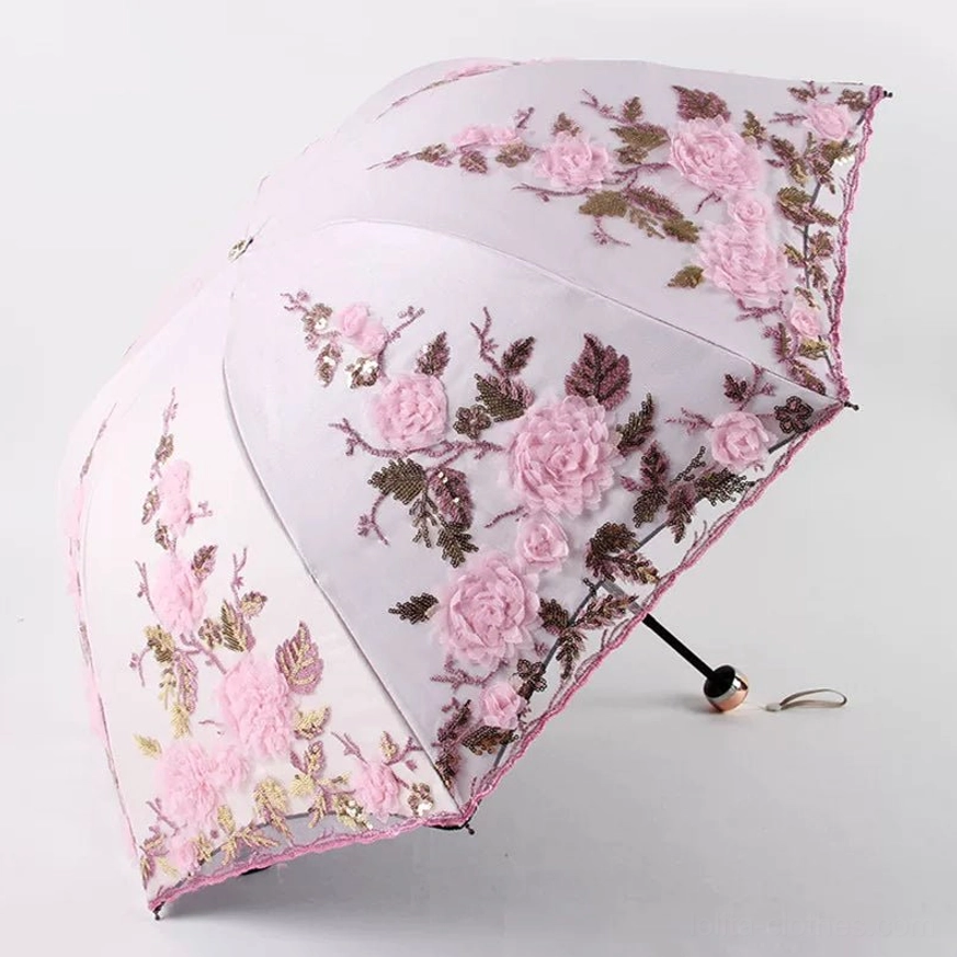 Light pink foldable lolita floral parasol with three-dimensional pink roses and dark burgundy leaf embroidery, pink scalloped lace trim, simple metal handle, fully opened from three-quarter top view against plain white studio background
