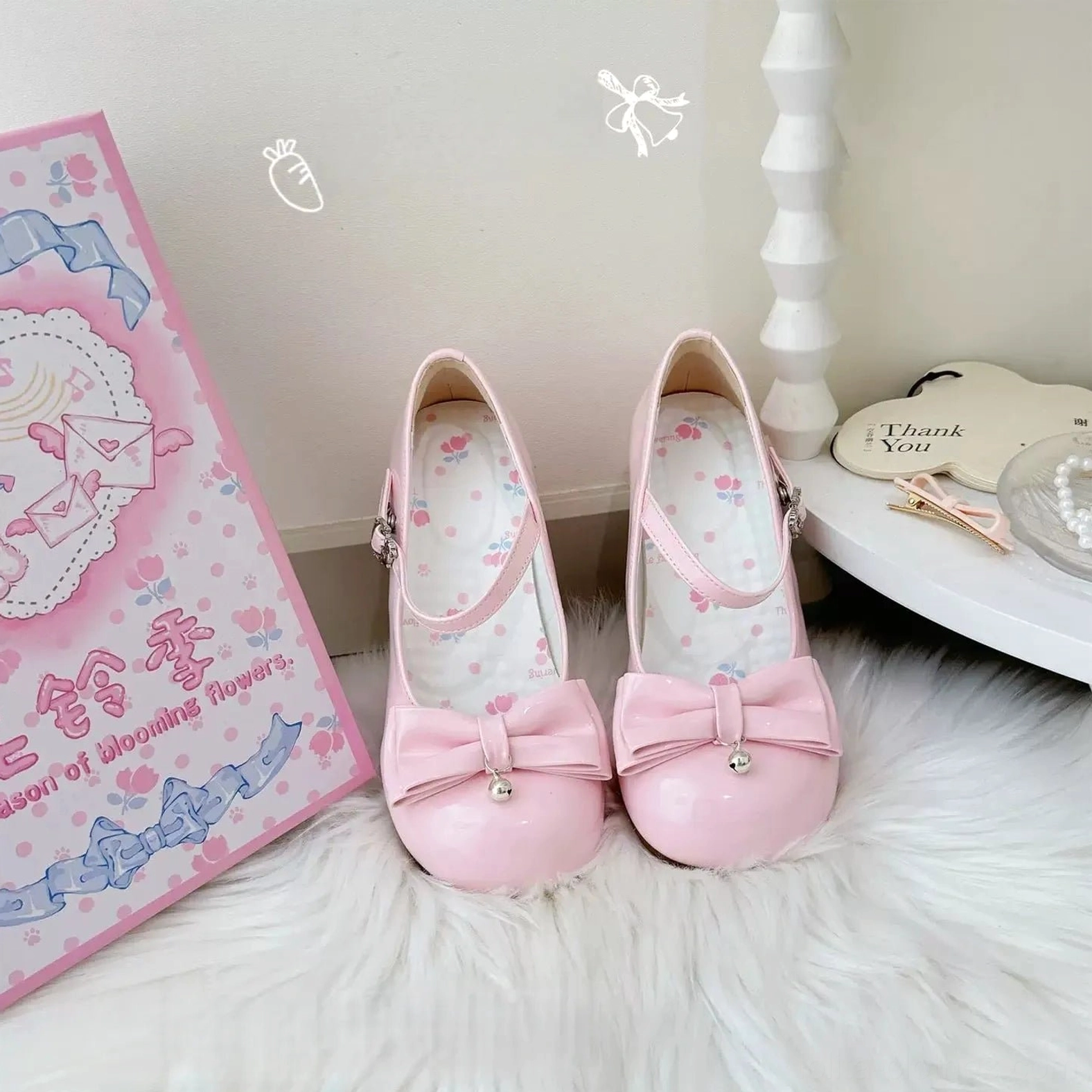 Light pink sweet lolita Mary Jane shoes on white fur rug featuring round toe silhouette, pearl-adorned front bow, adjustable ankle buckle strap, delicate floral printed insole, low block heel structure, displayed with branded packaging and vintage-inspired vanity decor