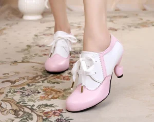 Light pink and white pastel two-tone Lolita retro high heel shoes with scalloped edge trim, curved spool heel, and metal-tipped ribbon lace fasteners, worn on indoor floral carpet