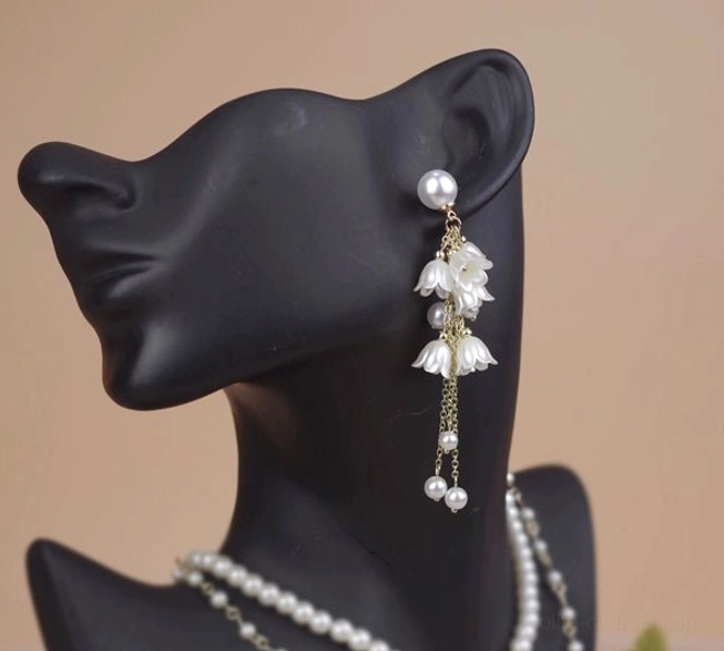 Single pair of lily flower dangle earrings side close-up view on ear mannequin showing round pearl stud cascading lily flower charms fine gold chain with dangling pearl accents