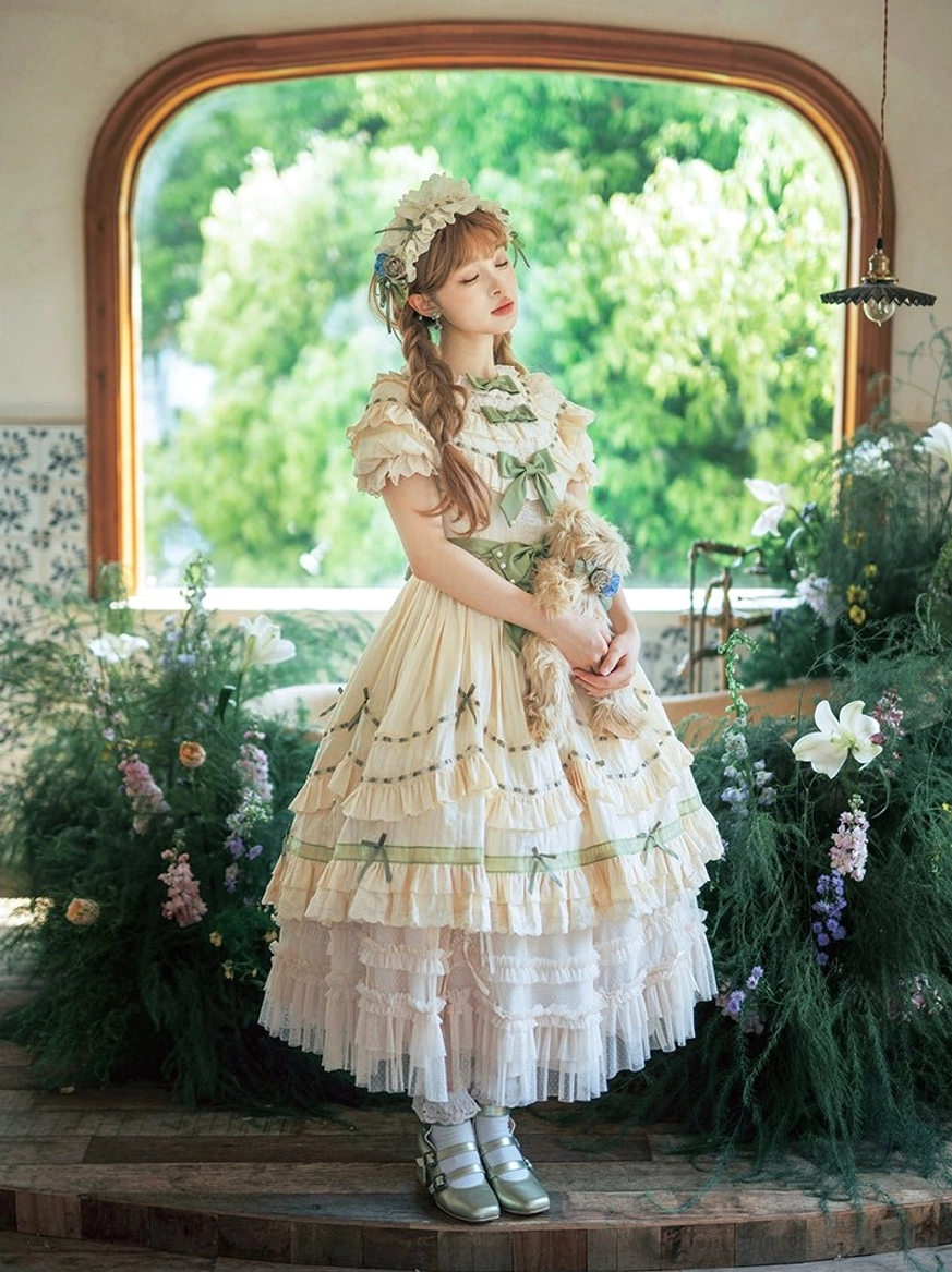 Lily of the valley country lolita OP dress with tiered ruffles and sage green ribbon accents shown from front standing view in vintage garden setting with arched window