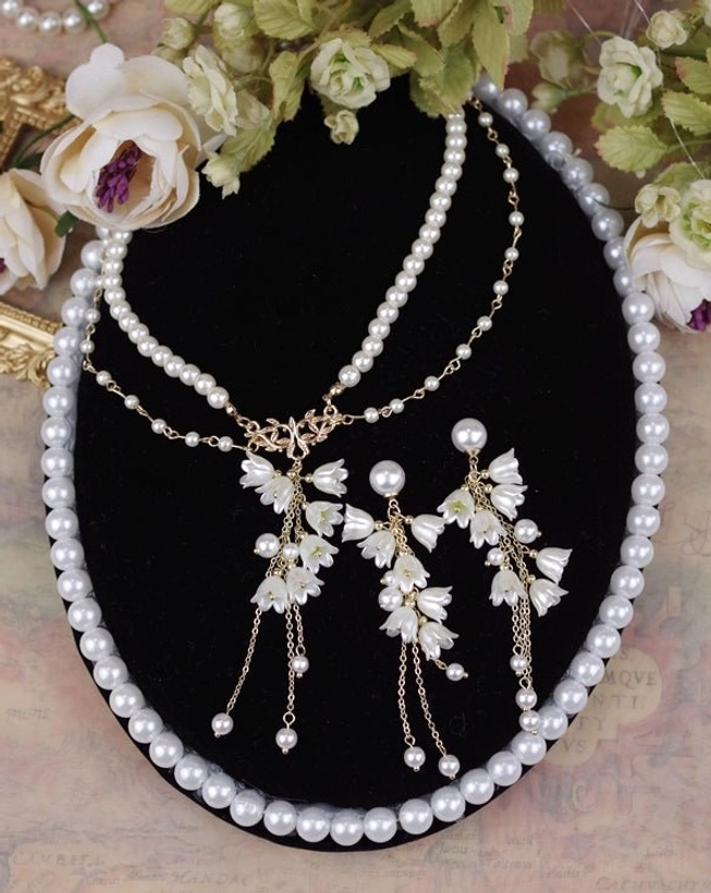 Elegant lily of the valley pearl Lolita jewelry set featuring layered necklace with pearl strands gold chain and matching pearl stud earrings displayed with vintage roses and loose pearls on beige background
