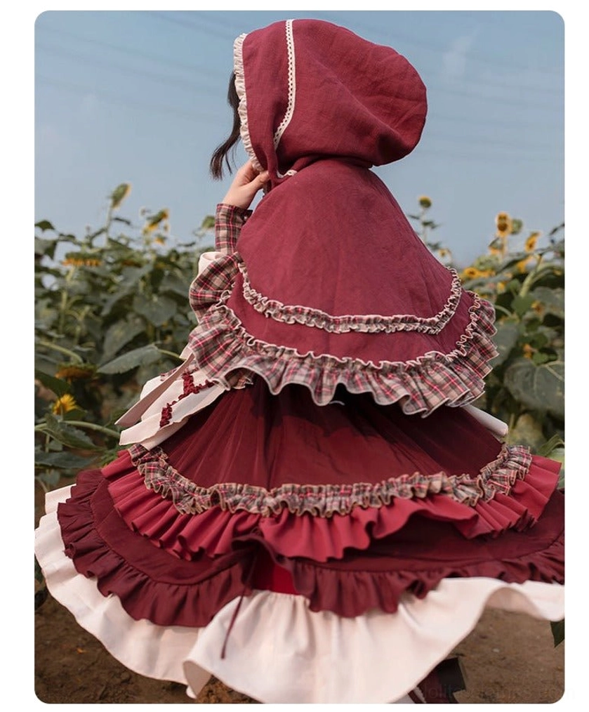 Hooded cloak with pastoral Lolita OP dress coordinate showing complete silhouette with lace-trimmed hood, ruffled cape edges, and multi-layered ruffled dress hem in outdoor setting