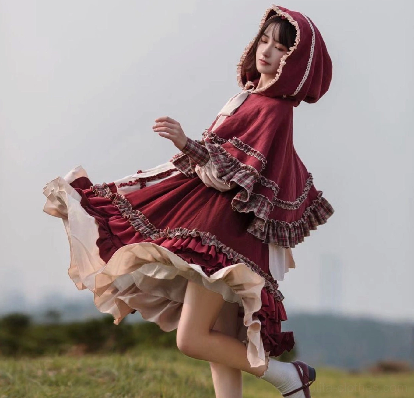Hooded cape with pastoral Lolita OP dress set, full-body side back view of model wearing flowing ruffled cape with lace-trimmed hood and layered ruffled skirt in grassland pasture setting