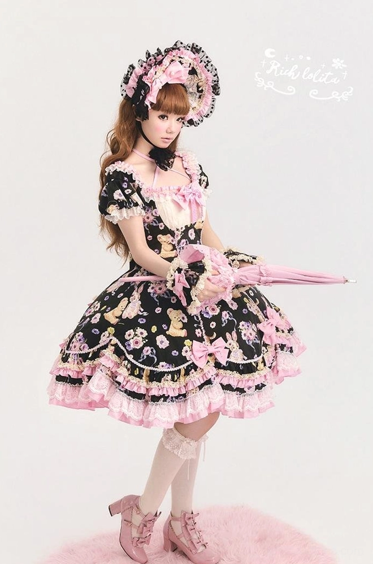 Full-body side front view of black sweet lolita OP dress with matching lace bonnet, open pink lace parasol, pink ruffled trims and bow decorations, studio pink rug backdrop