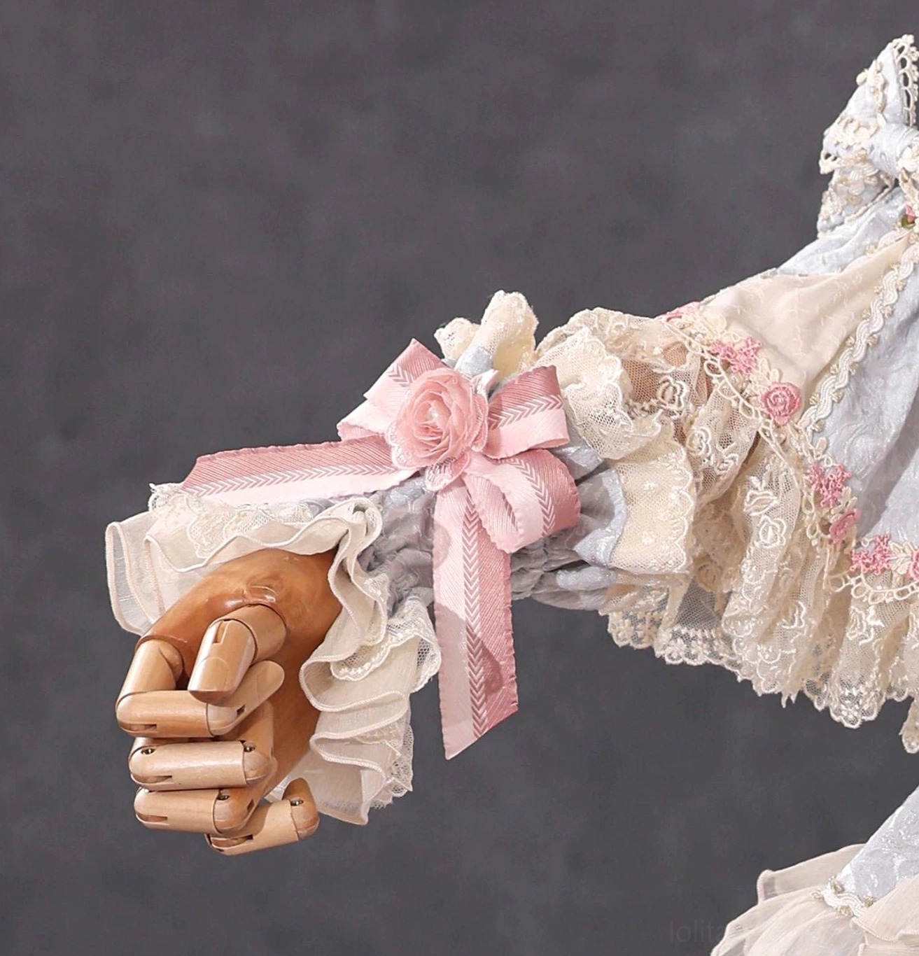 Beige cream lolita ruffled cuff with large pink satin bow, fabric rose accent, and frilled lace trim on wooden mannequin hand
