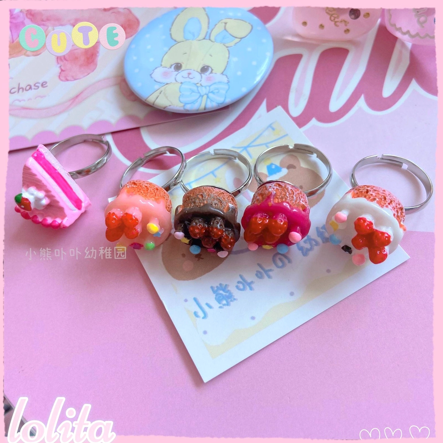 Pastel lolita aesthetic flat lay featuring dessert rings with cute bunny accessories and daisies on pink themed background