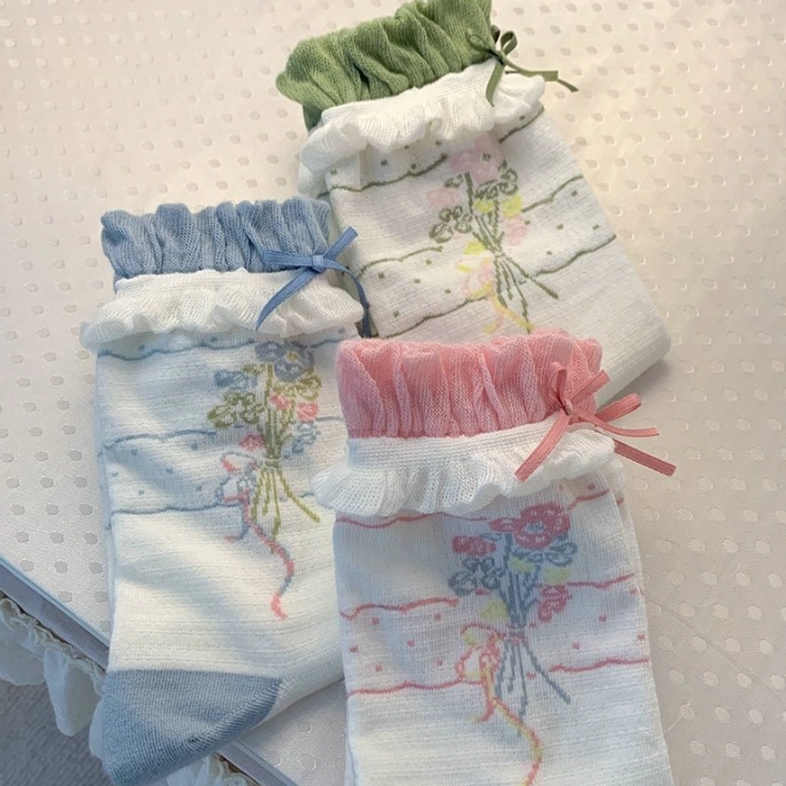 Three pairs of roji roji lolita ankle socks in blue pink and green color sets front flat lay close-up on polka dot fabric background showing floral bouquet prints ruffled cuffs matching bows
