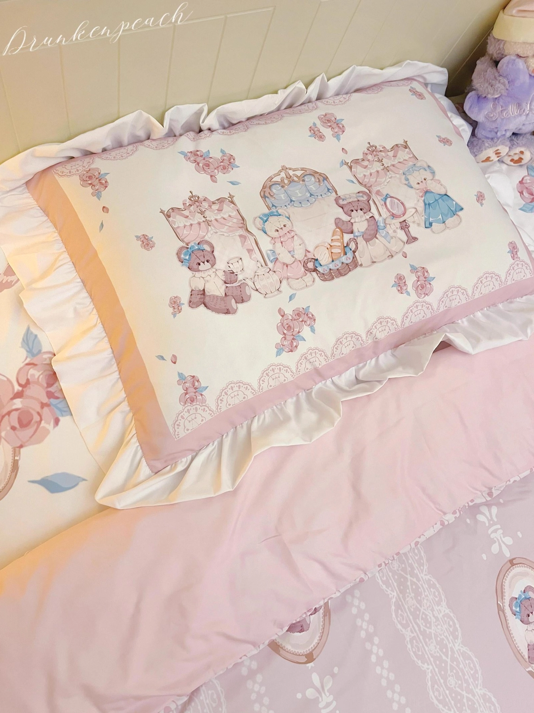 Low three-quarter side view of large ruffled pillow sham and matching lolita bedding with wide pink-trimmed ruffled pillow edge, detailed bear afternoon tea artwork, solid pink bed runner, and delicate lace sheet details