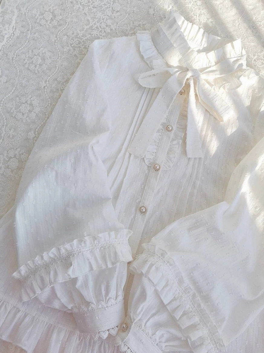 Lolita blouse angled overhead shot lace fabric background soft lighting ruffled cuffs pearl front bow neck detail cotton