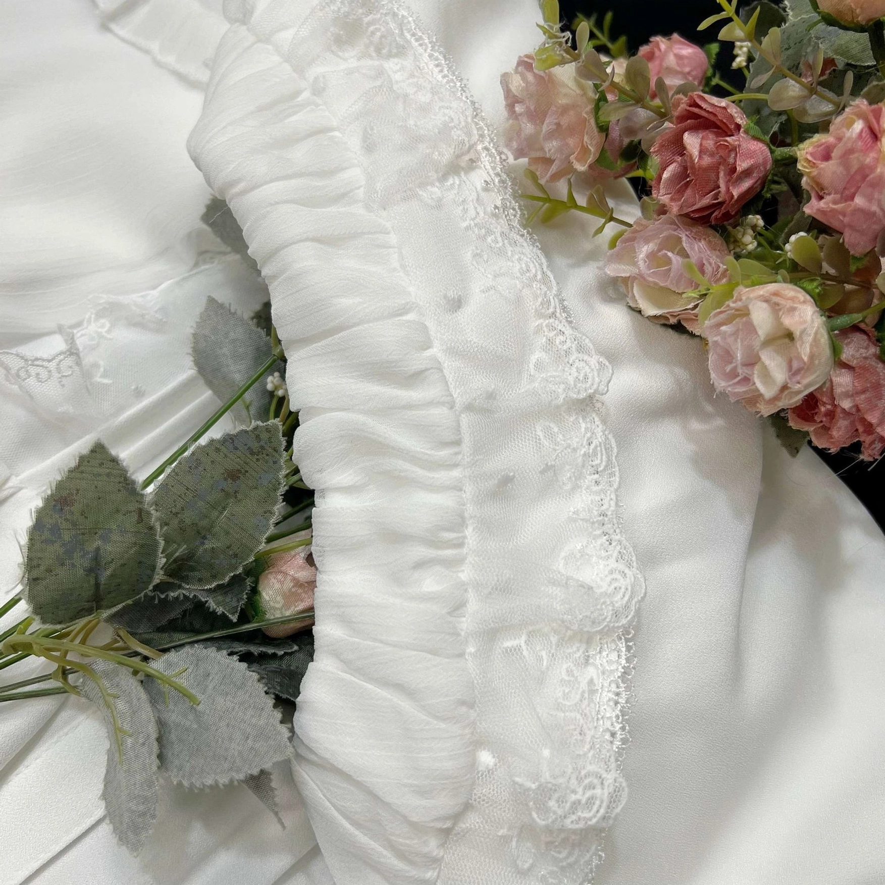 Close-up view of sweet Lolita blouse's front lace pintuck detail showing vertical fabric pintucking with ruffled lace trim accents surrounded by artificial roses