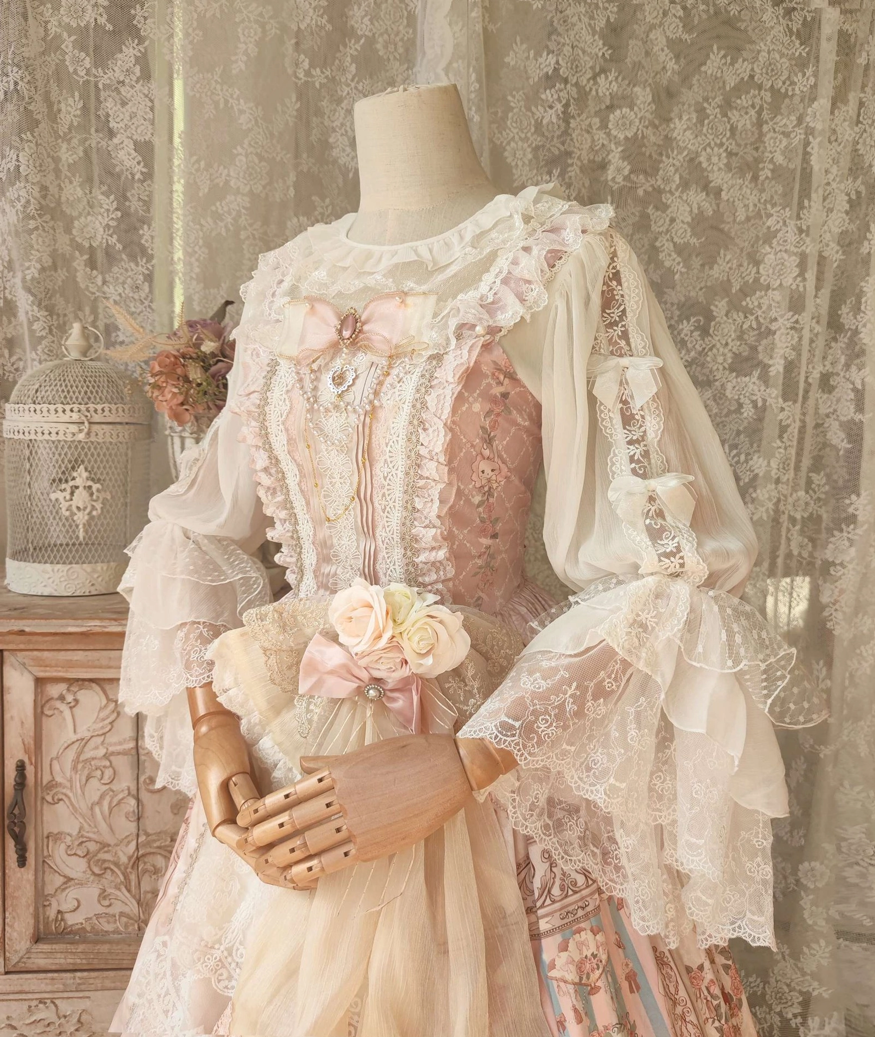 Full-front view of Lolita blouse with sheer overlay ruffled round neck layered lace sleeves and flower waist decoration in vintage indoor retro setting on dress form