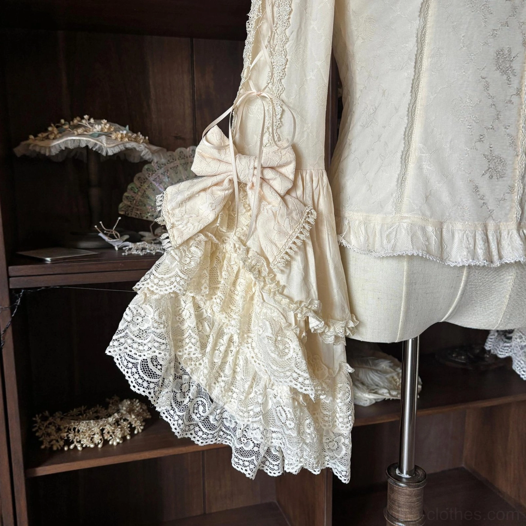 Close-up side view of classic lolita blouse sleeve showing large ruffled lace bell sleeve with big satin bow overlay and delicate cream-colored fabric texturing