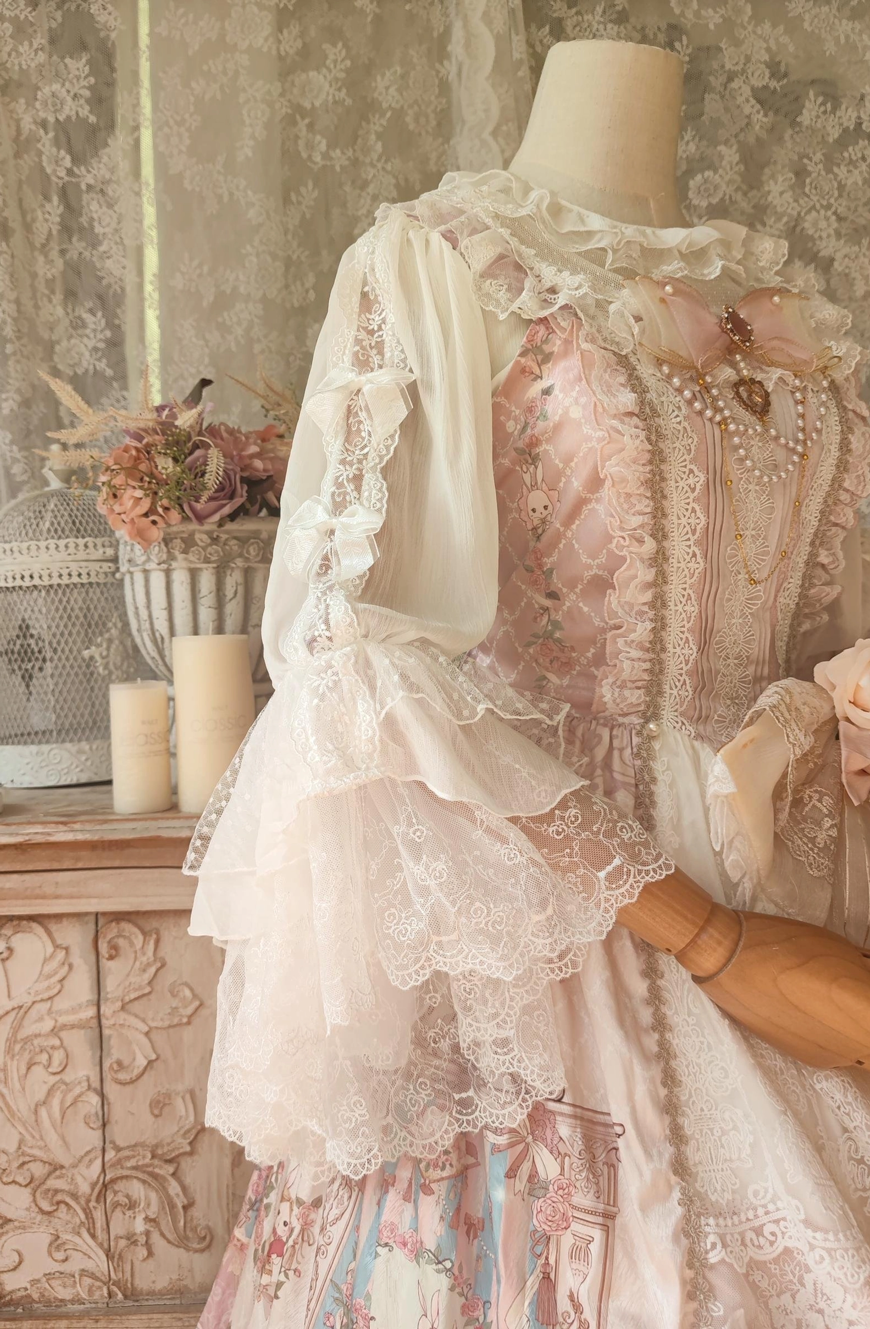 Close-up right side detail view of Lolita blouse showing trumpet lace sleeves and intricate lace embroidery on cream-pink bodice with vintage cabinet background