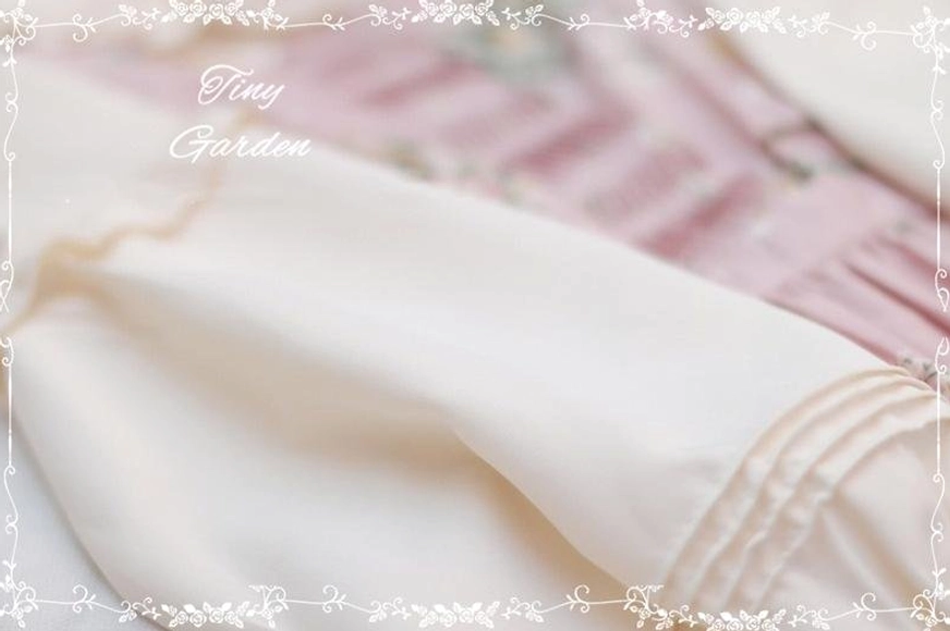 Lolita blouse sleeve cuff detail close-up showing ruffled flared edge with pin-tuck pleated trim against blurred pink floral background