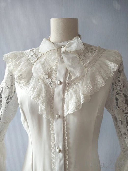 Close-up detail of white Lolita blouse upper body featuring ruffled lace yoke, pearl buttons, detachable neck bow, and sheer floral lace long sleeves on dress form