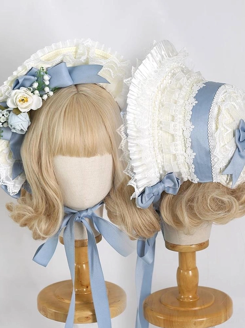 Blue and ivory lolita lace bonnet headdress with ruffled lace trim, dusty blue satin bows, and artificial rose floral accents displayed on blonde wig mannequin