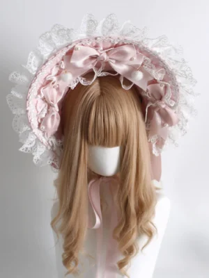 Classic Lolita bonnet headdress front view, featuring ruffled white lace border, pink satin bows, pom-pom details, and matching neck ribbon on blonde wig mannequin