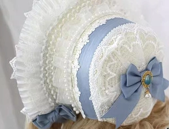 Close-up detail of lolita bonnet showing ivory lace fabric texture, blue satin band with gemstone pendant, and ruffled edge trim