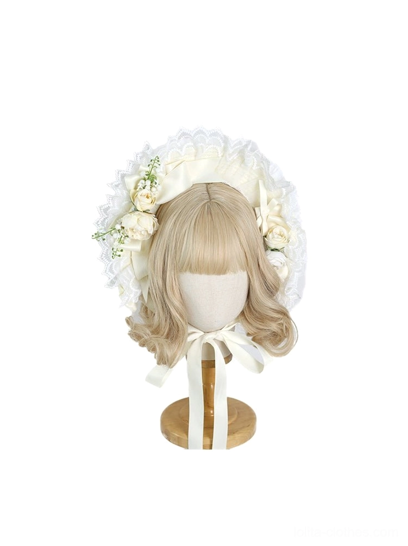 Miniature cream lolita bonnet headdress on tiny blonde wig mannequin with artificial flowers and matching cream neck tie straps on wooden display stand