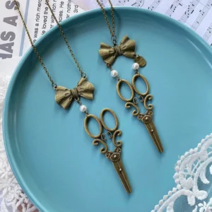 Antique bronze Lolita bow-scissors necklace showing two variants with pearl and scissor pendants on vintage newspaper background with ceramic tray, classic sweater chain style