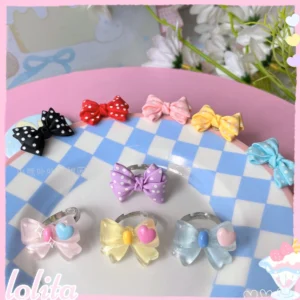 Close-up overhead view of assorted kawaii bowknot finger rings on blue and white checkered ceramic plate showing polka dot and solid bow designs with metal adjustable bases