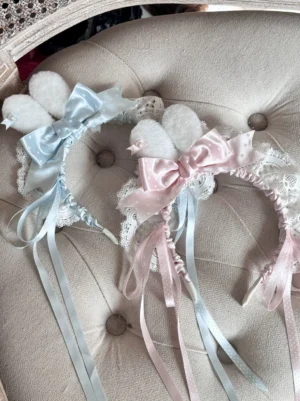 Lolita bunny ear headdress flat lay overhead view on beige upholstered sofa, showing satin bows and delicate lace edging with long hanging ribbons
