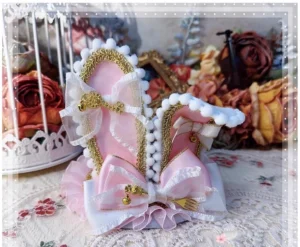 Platinum pink lolita bunny ear top hat headdress with ribbon bow and gold metal charm on vintage lace tabletop with dried flowers, front view