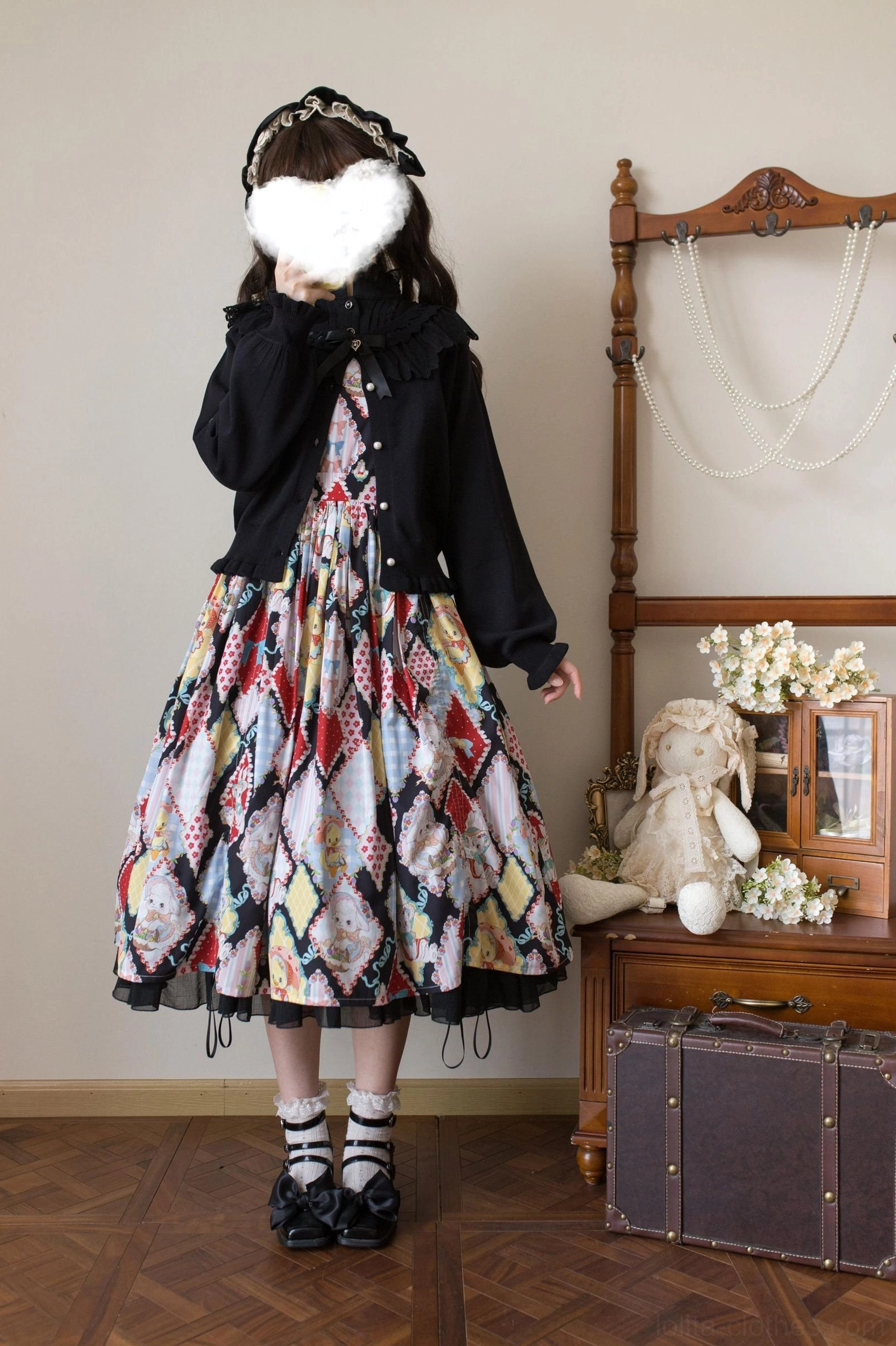 Full body model shot of black lolita cardigan worn with printed midi skirt and hairband accessory in cozy vintage interior setting with wooden furniture and decorative accents
