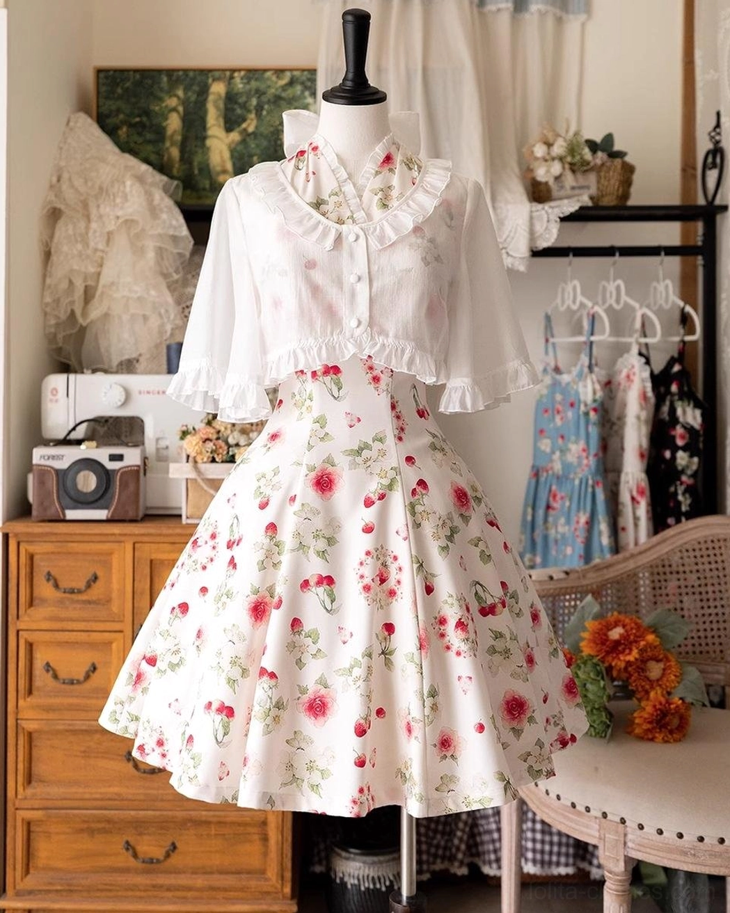 Three-quarter view Lolita outfit showing white ruffled short cardigan layered over white base with red floral midi dress, cape-style cropped silhouette and full A-line skirt on dress form