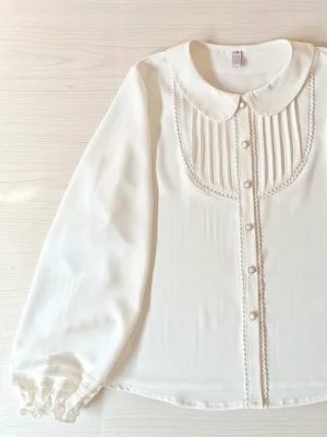 flat lay overhead view white lolita blouse with pearl front buttons lace-trimmed pintuck panel and classic doll collar on light wood surface