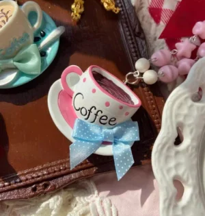 Close-up overhead view of Lolita coffee cup pendant necklace with polka dot teacup charm and blue bow on dark wooden tray with red checkered background