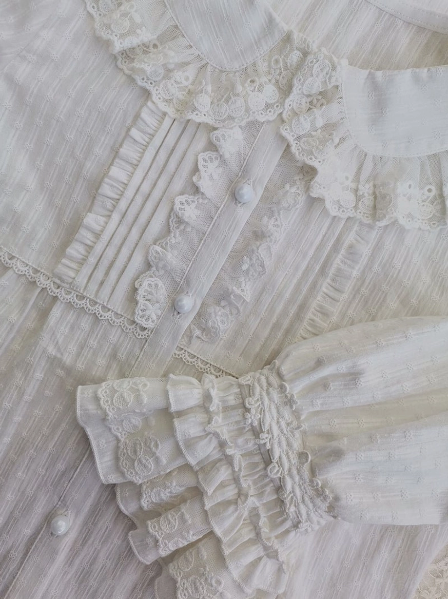 Overhead close-up view of white lolita blouse front round buttons, lace-trimmed pleated tucks, layered ruffle lace cuff, and intricate lace embroidery details on cotton fabric