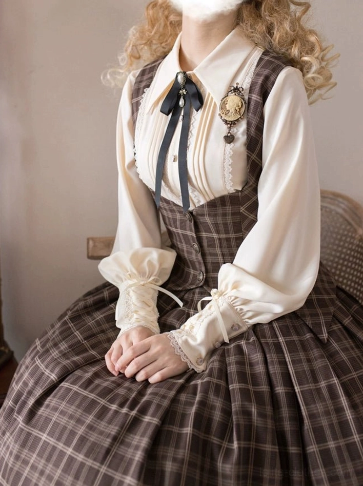 Classic Lolita daily coordinate featuring white pleated pointed collar shirt with ruffled cuffs, black bow tie and vintage brooch, paired with brown plaid suspender skirt, seated indoor home studio perspective
